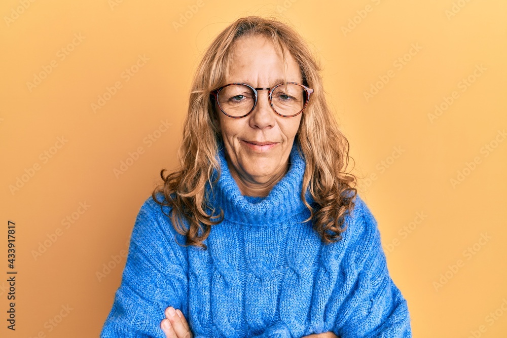 Middle age blonde woman wearing glasses and casual winter sweater happy face smiling with crossed arms looking at the camera. positive person.