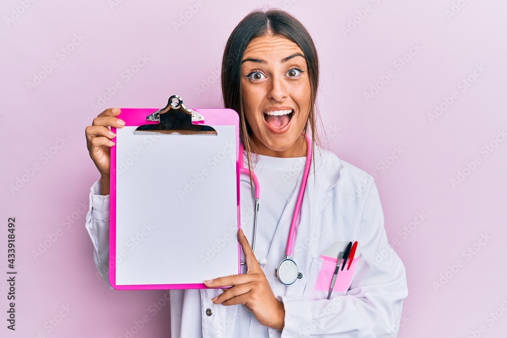 Beautiful hispanic woman wearing doctor stethoscope holding clipboard celebrating crazy and amazed for success with open eyes screaming excited. Beautiful hispanic woman wearing doctor stethoscope holding clipboard celebrating crazy and amazed for success with open eyes screaming excited.
