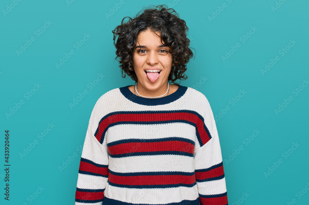 Young hispanic woman with curly hair wearing casual clothes sticking tongue out happy with funny expression. emotion concept. Young hispanic woman with curly hair wearing casual clothes sticking tongue out happy with funny expression. emotion concept.