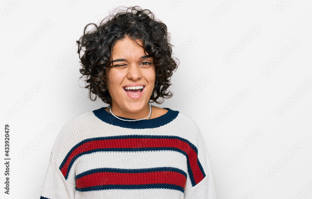 Young hispanic woman with curly hair wearing casual clothes winking looking at the camera with sexy expression, cheerful and happy face. Young hispanic woman with curly hair wearing casual clothes winking looking at the camera with sexy expression, cheerful and happy face.