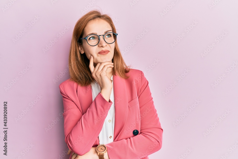Young caucasian woman wearing business style and glasses with hand on chin thinking about question, pensive expression. smiling and thoughtful face. doubt concept.