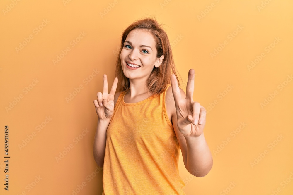 Young caucasian woman wearing casual style with sleeveless shirt smiling looking to the camera showing fingers doing victory sign. number two. Young caucasian woman wearing casual style with sleeveless shirt smiling looking to the camera showing fingers doing victory sign. number two.