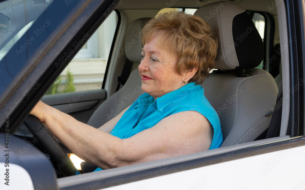 Obraz premium Beautiful lady in a blue shirt in her 70s is driving a car