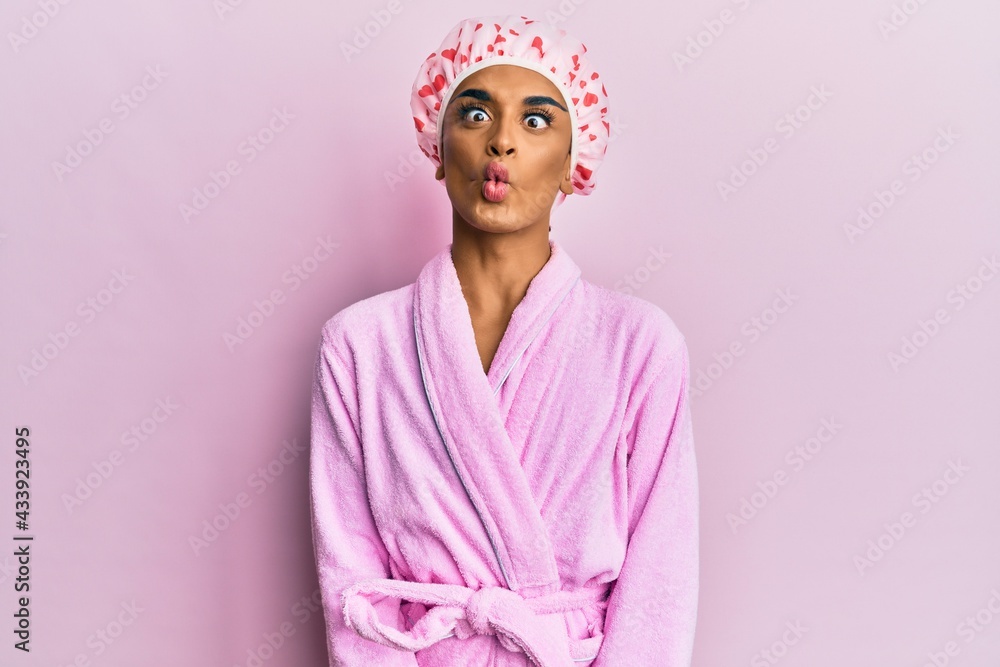 Hispanic man wearing make up wearing shower towel cap and bathrobe making fish face with lips, crazy and comical gesture. funny expression. Hispanic man wearing make up wearing shower towel cap and bathrobe making fish face with lips, crazy and comical gesture. funny expression.