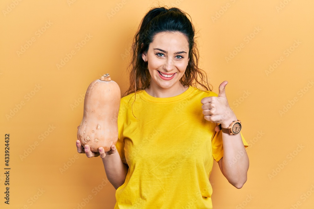 Young hispanic woman holding healthy fresh pumpkin smiling happy and positive, thumb up doing excellent and approval sign Young hispanic woman holding healthy fresh pumpkin smiling happy and positive, thumb up doing excellent and approval sign