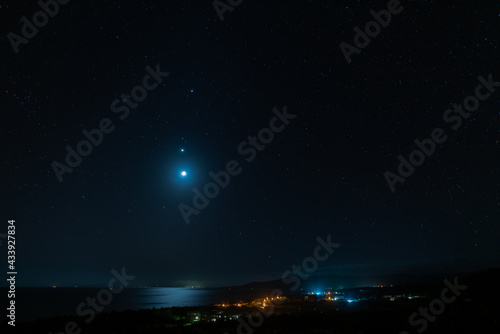 Amazing twilight starry sky, the moon reflecting in the sea, Venus and Jupiter composing the beautiful night scene view from above of the city of Uehara. Iriomote Island.