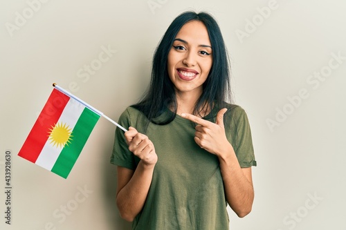 Tablou pe pânză Young hispanic girl holding kurdistan flag smiling happy pointing with hand and