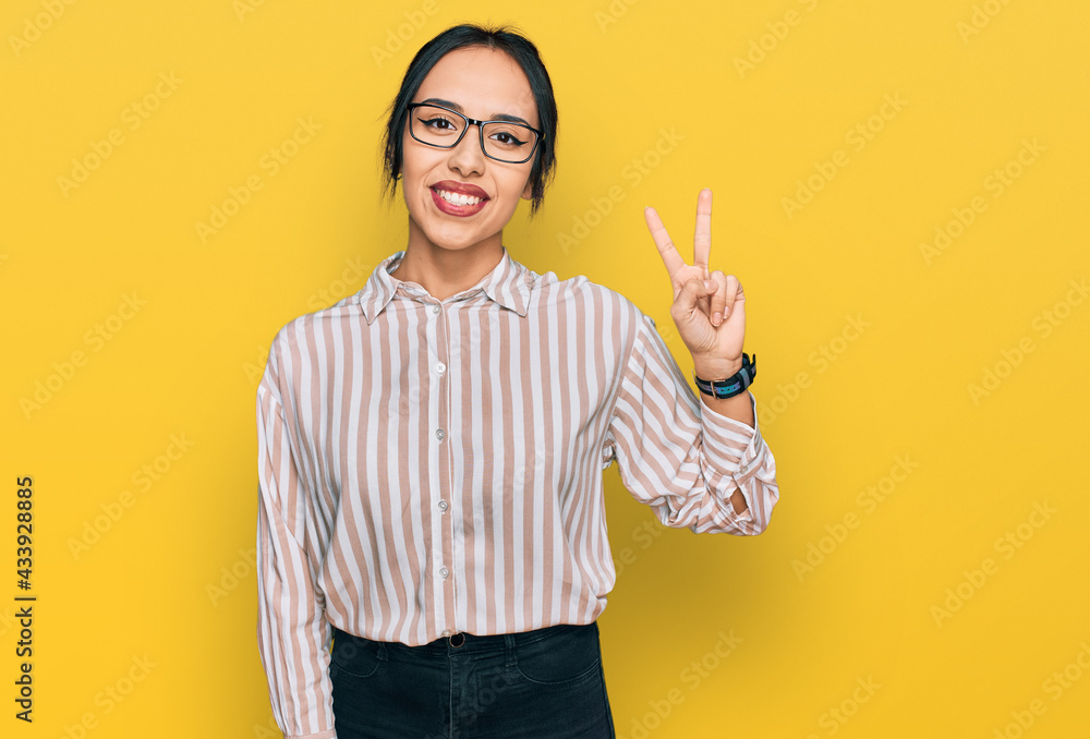 Young hispanic girl wearing casual clothes and glasses smiling looking to the camera showing fingers doing victory sign. number two. Young hispanic girl wearing casual clothes and glasses smiling looking to the camera showing fingers doing victory sign. number two.