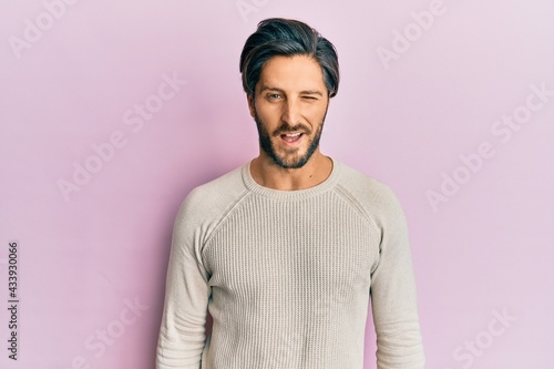 Young hispanic man wearing casual winter sweater winking looking at the camera with sexy expression, cheerful and happy face.