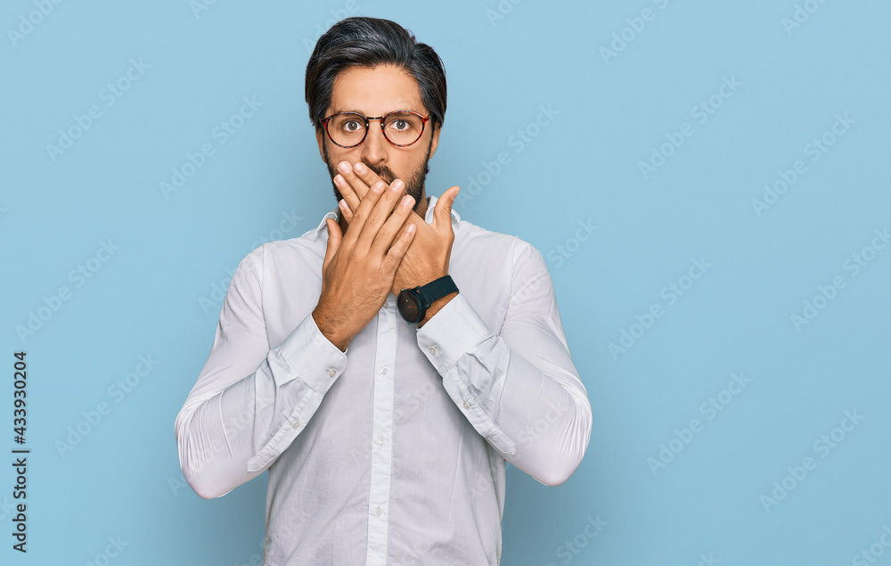 Young hispanic man wearing business shirt and glasses shocked covering mouth with hands for mistake. secret concept. Young hispanic man wearing business shirt and glasses shocked covering mouth with hands for mistake. secret concept.