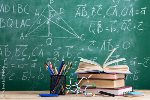 Education and sciences concept - books on the teacher desk in the auditorium, chalkboard on the background.