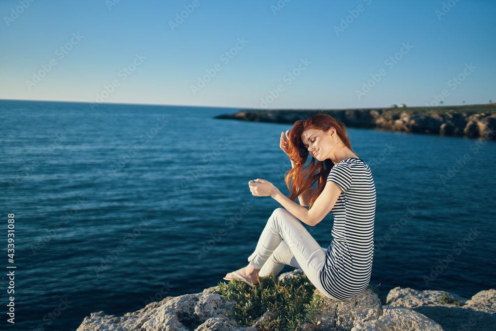 woman in a t-shirt and trousers sits on a rock on the beach near the sea top view woman in a t-shirt and trousers sits on a rock on the beach near the sea top view
