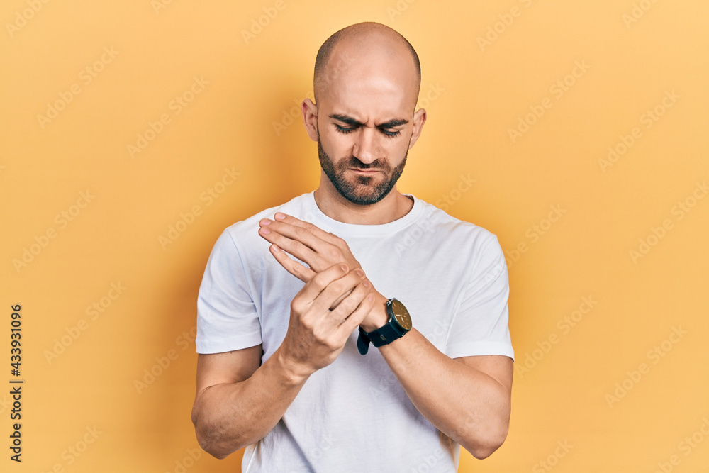 Young bald man wearing casual white t shirt suffering pain on hands and fingers, arthritis inflammation Young bald man wearing casual white t shirt suffering pain on hands and fingers, arthritis inflammation
