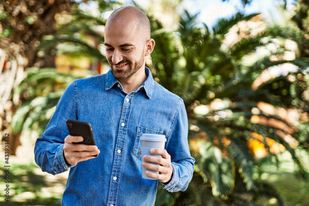 Fototapeta premium Young hispanic man using smartphone and drinking coffee at the park.