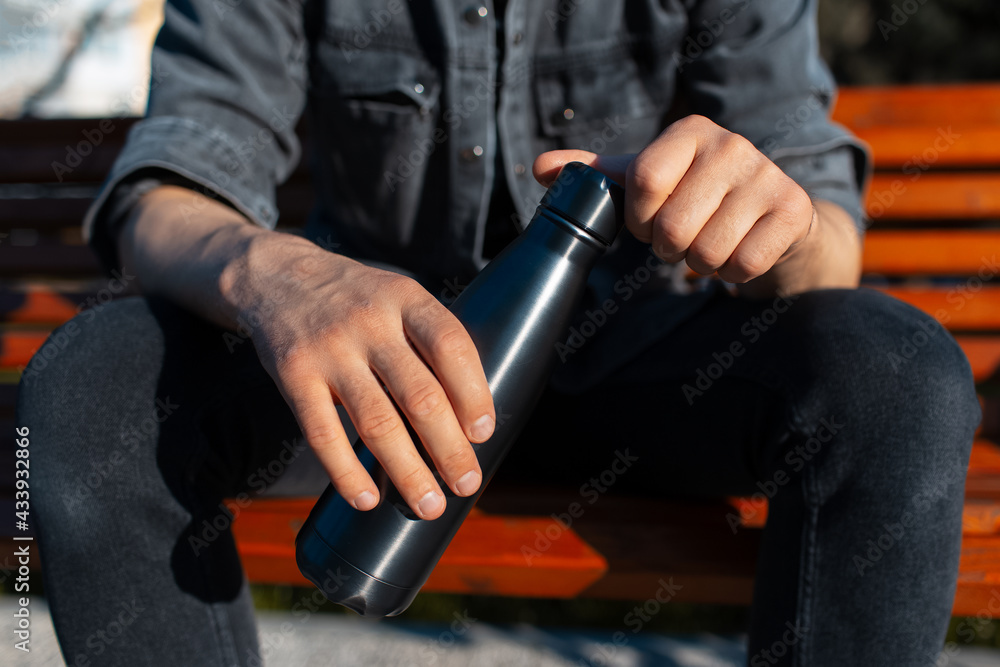 Naklejka premium Close-up of black steel stainless thermo water bottle in male hands. Reusable bottles concept. Zero waste.