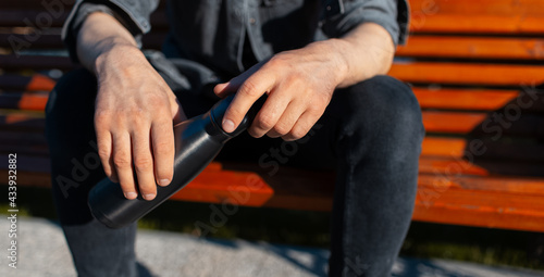 Close-up of male hands, holding steel reusable thermo water bottle.