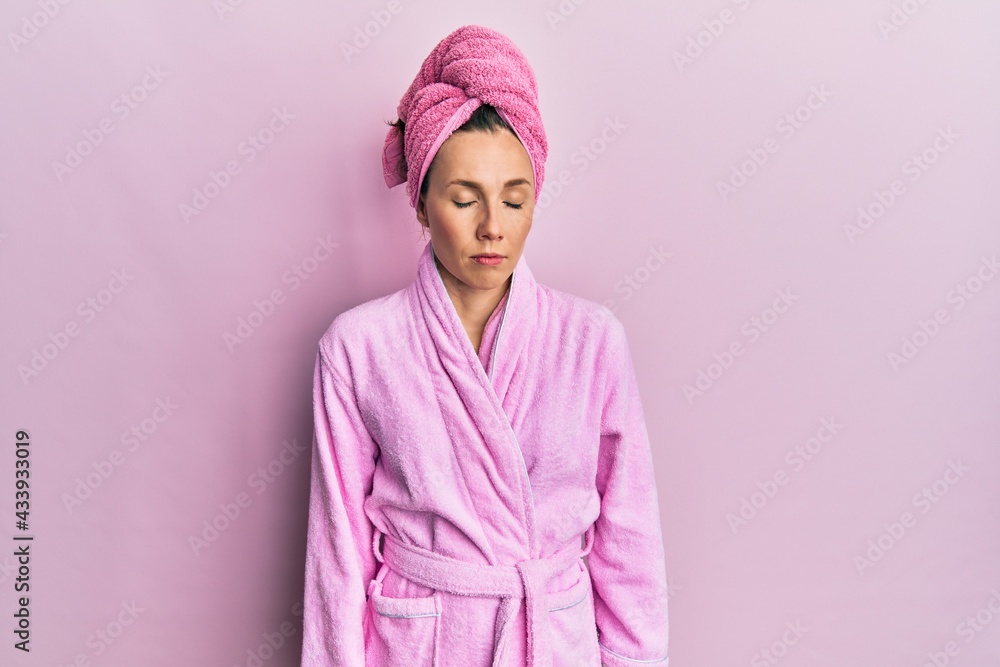 Fototapeta premium Young blonde woman wearing shower towel cap and bathrobe looking sleepy and tired, exhausted for fatigue and hangover, lazy eyes in the morning.