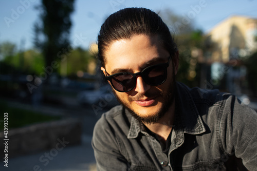 Outdoor portrait of young smiling man wearing sunglasses on background of blurred street.