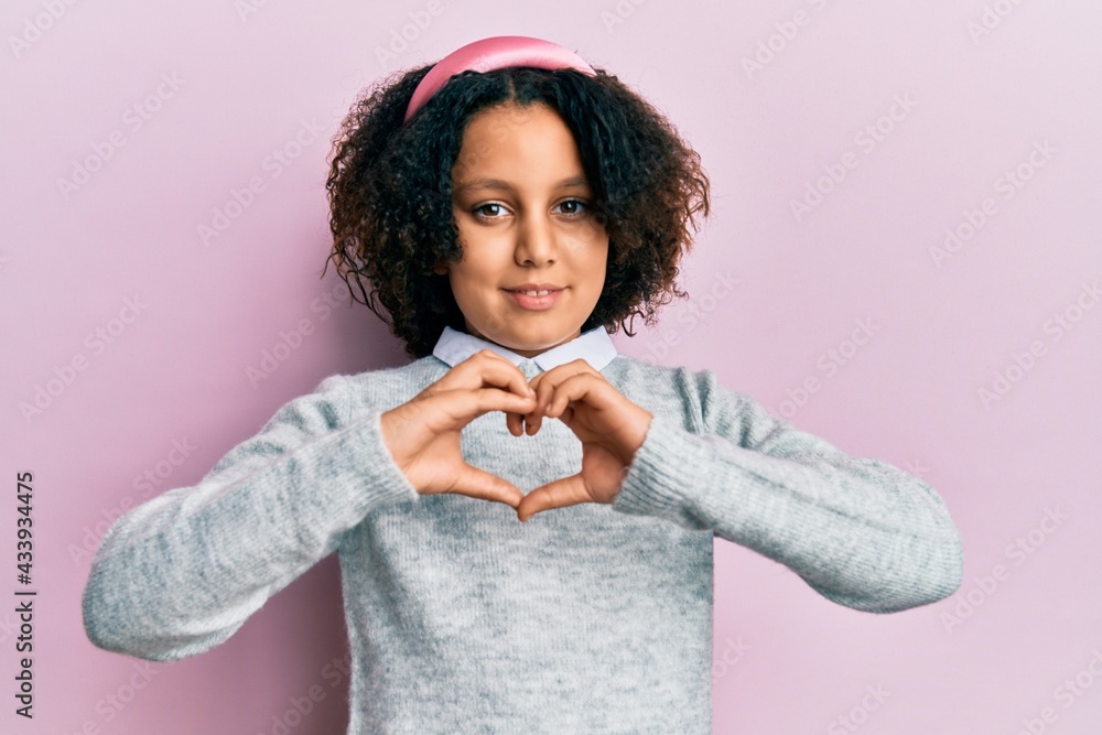 Young little girl with afro hair wearing casual clothes smiling in love showing heart symbol and shape with hands. romantic concept. Young little girl with afro hair wearing casual clothes smiling in love showing heart symbol and shape with hands. romantic concept.