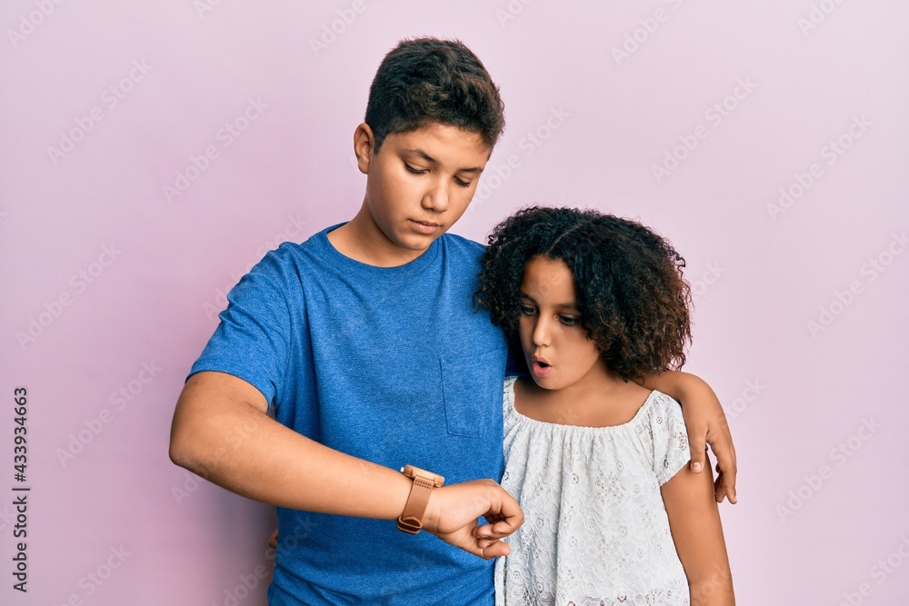 Young hispanic family of brother and sister wearing casual clothes together checking the time on wrist watch, relaxed and confident Young hispanic family of brother and sister wearing casual clothes together checking the time on wrist watch, relaxed and confident