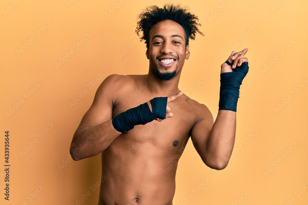Fototapeta premium Young african american man with beard using boxing protection smiling and looking at the camera pointing with two hands and fingers to the side.