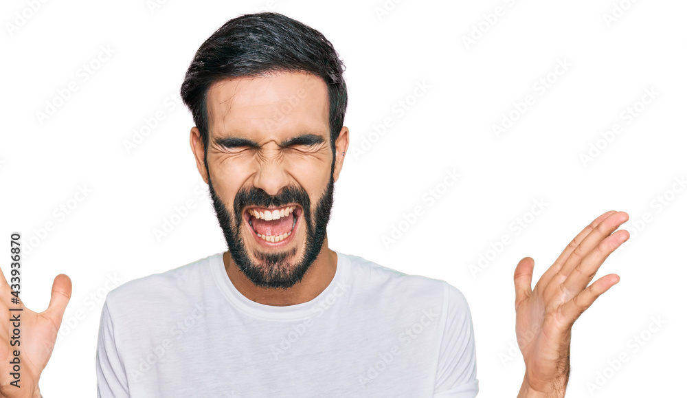 Young hispanic man wearing casual white t shirt celebrating mad and crazy for success with arms raised and closed eyes screaming excited. winner concept Young hispanic man wearing casual white t shirt celebrating mad and crazy for success with arms raised and closed eyes screaming excited. winner concept