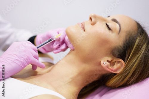 Doctor injecting hyaluronic acid into the ching of a woman as a facial rejuvenation treatment.