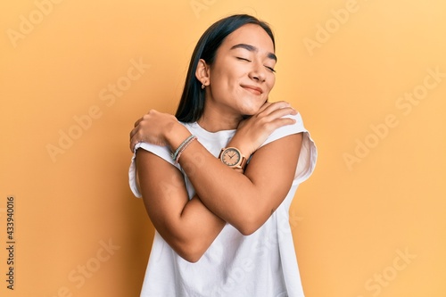 Fotografie Young asian woman wearing casual white t shirt hugging oneself happy and positive, smiling confident