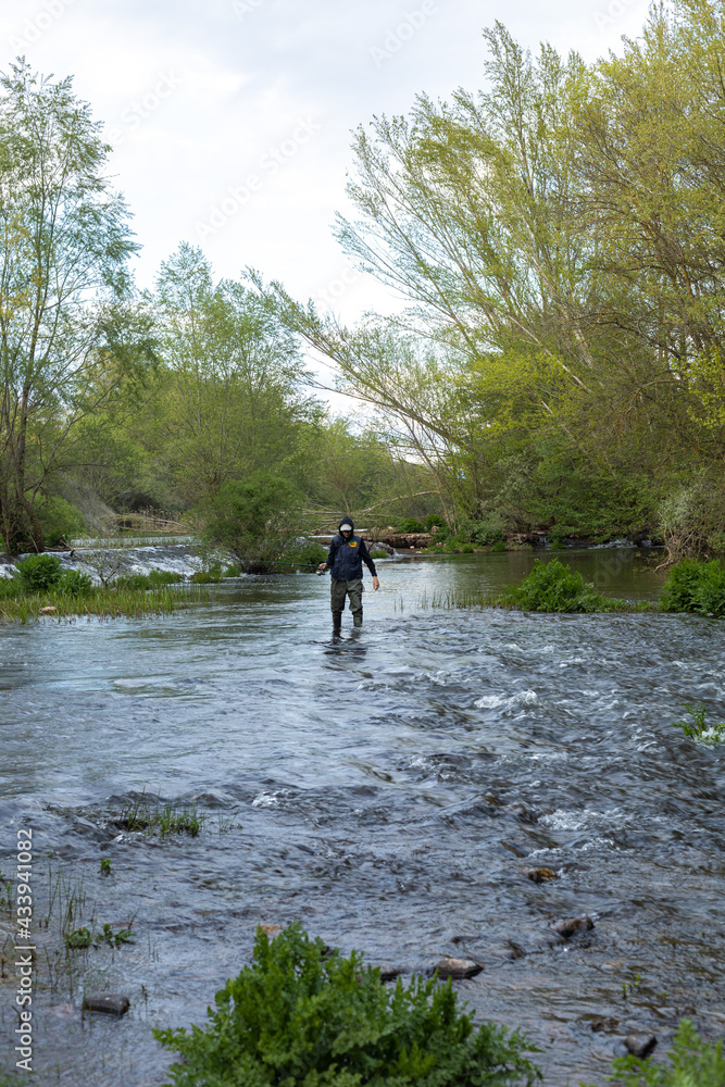 Obraz premium young angler in the middle of the river with a fishing rod and appropriate clothing for the sport wading in the stream in search of fish to catch