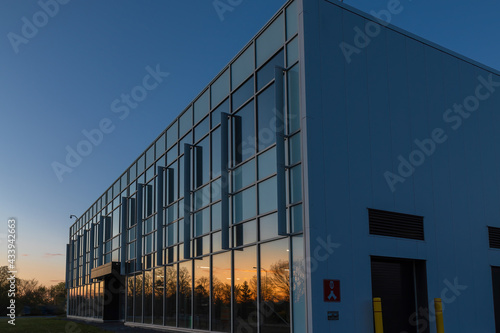 Low-rise commercial or institutional building glass and aluminum facade at dusk with sunset reflecting on windows, security cameras, nobody photo
