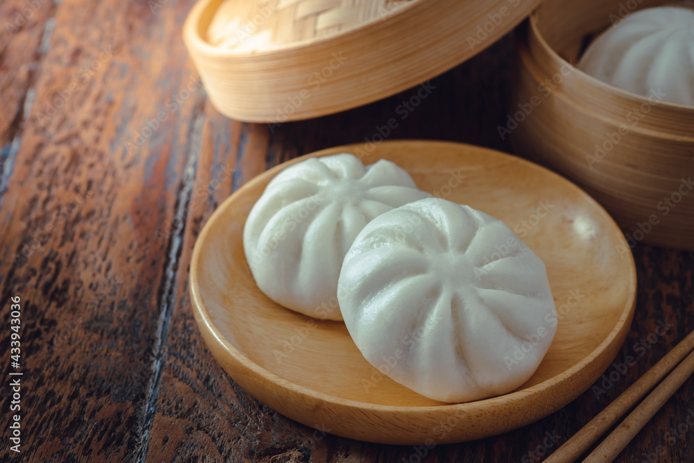 Steamed pork buns on wooden plate and bamboo steamer, Chinese dim sum Steamed pork buns on wooden plate and bamboo steamer, Chinese dim sum