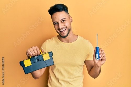 Young arab man holding toolbox and screwdriver smiling and laughing hard out loud because funny crazy joke.