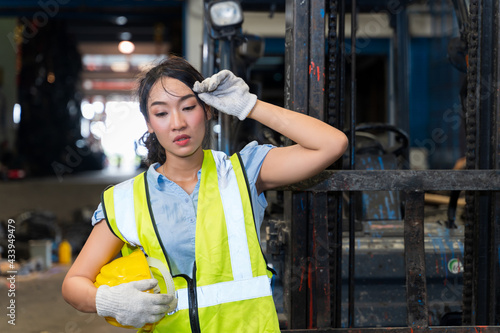 The female engineer was tired from work, was wiping her hands, wiping sweat on her face and standing at the forklift in a factory in Industrial Engineering worker concept.