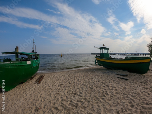 Fototapeta Naklejka Na Ścianę i Meble -  Two colorful boats parked on the sandy beach in Gdynia, Poland. In the back there is a small pier going into the calm Baltic Sea. Thick, white clouds on the blue sky. Fishing boats.