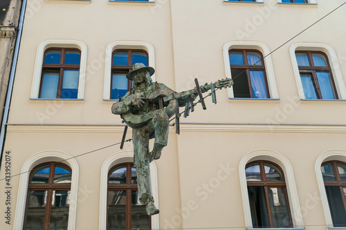 A figure of a man playing the guitar handed above the street in Katowice, Poland. In the back there is a tall building. The monument is handed on a metal rope. Modern art.