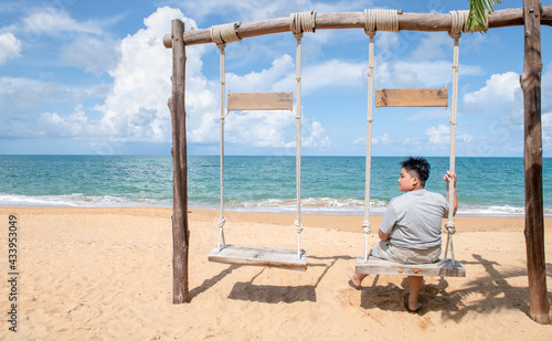 Happy tourist sit and relax on the wooden swing in front of the beach, relax and rest