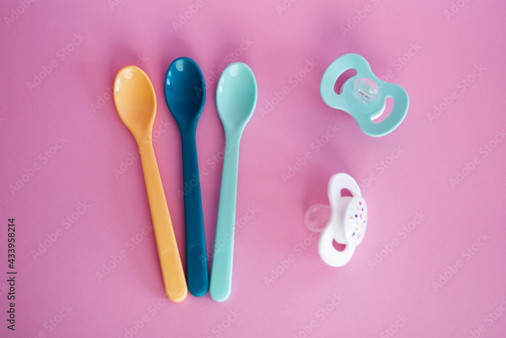 Baby plastic spoons and pacifiers in pastel colours. Baby accessories on pink background, top view. Cutlery for children. Baby plastic spoons and pacifiers in pastel colours. Baby accessories on pink background, top view. Cutlery for children.