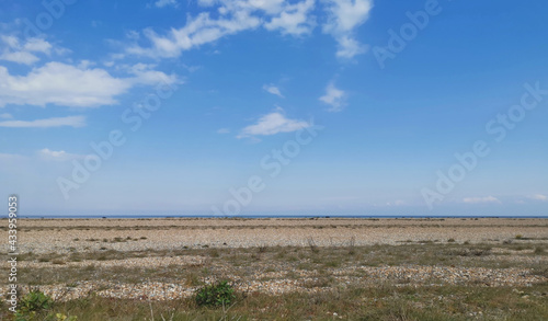 Deserted marshland beach with rough ground in foreground and sea on horizon
