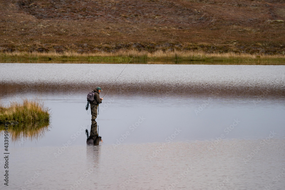 Fisherman alone stand in river water. Hobby sport activity. Fisherman fishing equipment. Reflection in Loch Long.