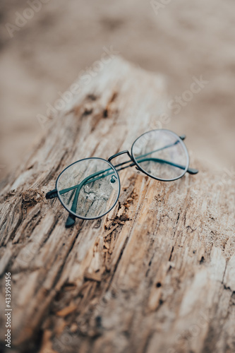 Womens beautiful glasses lie on a narrow beam on the beach on a blurred background