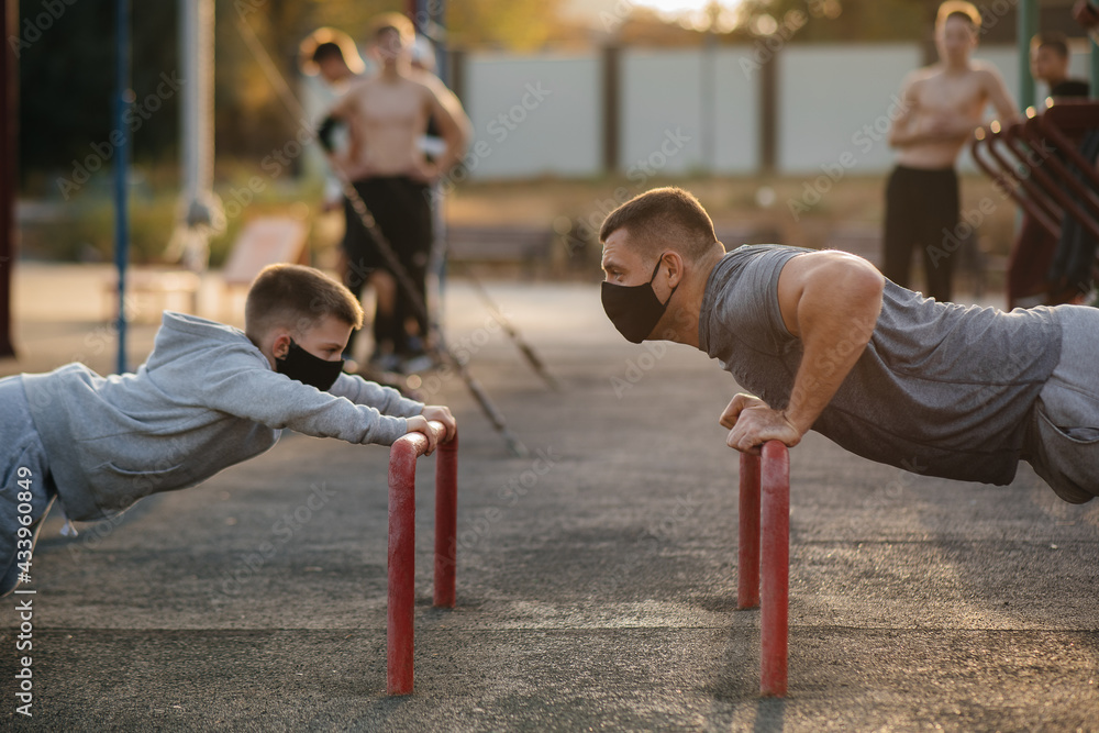 Fototapeta premium Father and son play sports on the sports field in masks during sunset. Healthy parenting and healthy lifestyle