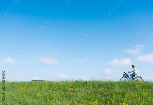 woman rides bicycle on grassy dike with flowers under blue sky