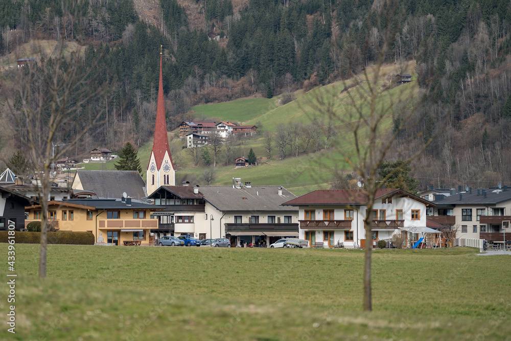 The church of St. Pankraz in Uderns, Zillertal valley, surrounded by green grass and snow with Alps mountains in the background in a landscape on a white winter evening in Austria.