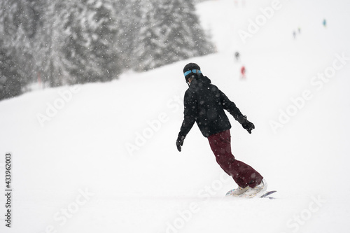 Unidentified tourist does snowboard skiing in Flachau, the ski resort in Austria. Man in black and red sportswear. Foggy weather.