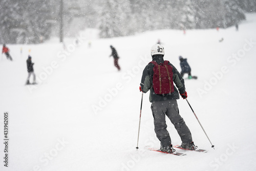 Unidentified tourist skiing in Flachau, the ski resort in Austria. Man in red sportswear. People on bokeh background. View from behind.