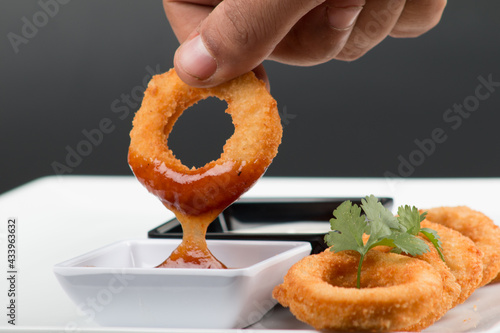 Aros de cebolla tomados con la mano y bañados en salsa photo