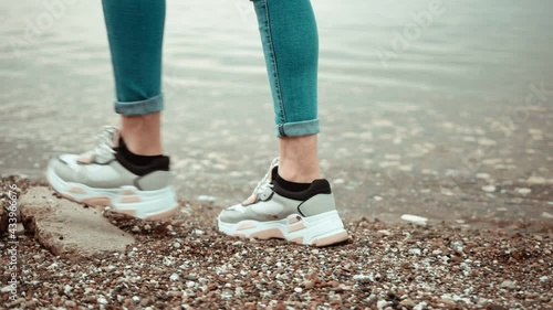 Legs of a girl walking on wet sand by the river. Close-up.