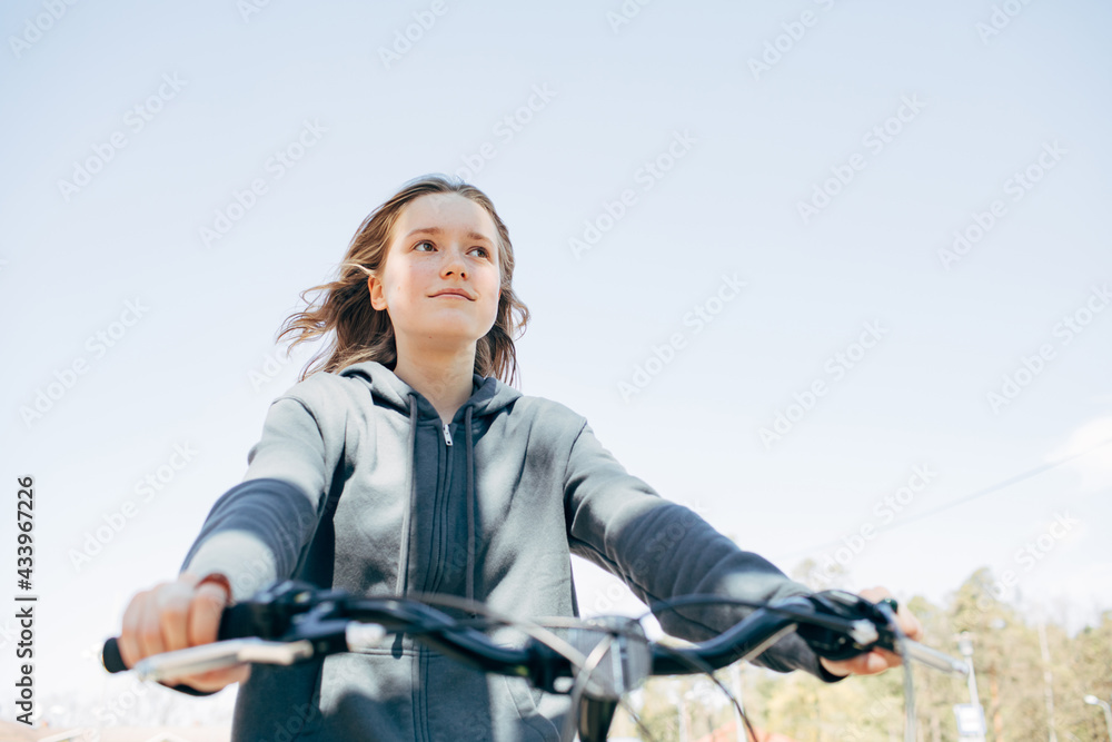 Teenager girl on a city bike. Portrait of a beautiful girl. Sunny summer weather. Casual blue hoody. Lifestyle people close up enjoying summer. Bicycle steer in a foreground Teenager girl on a city bike. Portrait of a beautiful girl. Sunny summer weather. Casual blue hoody. Lifestyle people close up enjoying summer. Bicycle steer in a foreground