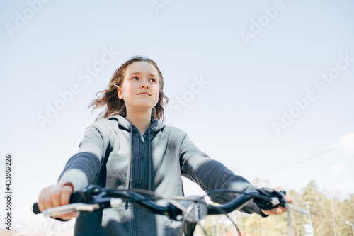 Teenager girl on a city bike. Portrait of a beautiful girl. Sunny summer weather. Casual blue hoody. Lifestyle people close up enjoying summer. Bicycle steer in a foreground