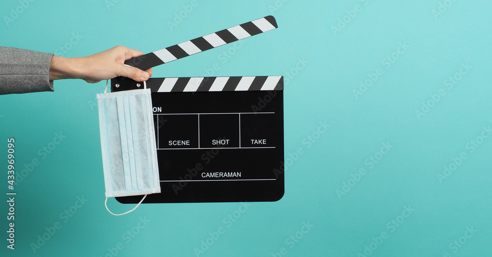 Hands with grey suit and hold black Clapper board or movie slate with face mask. it use in video production ,movies and cinema industry on blue and green or mint background.